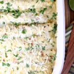Pan of pulled pork enchiladas topped with green chili sauce and cheese.